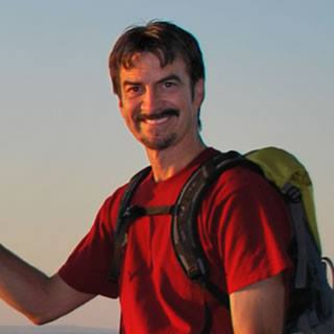 Headshot of Chuck Dovish outfitted in backpacking gear and a red T-shirt